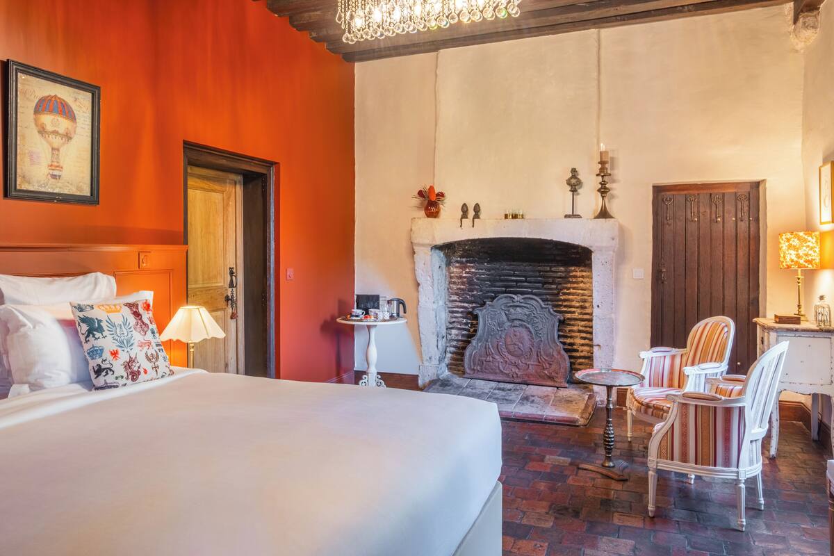 Een hotelkamer met een groot bed, een open haard en een zithoek met stoelen.
