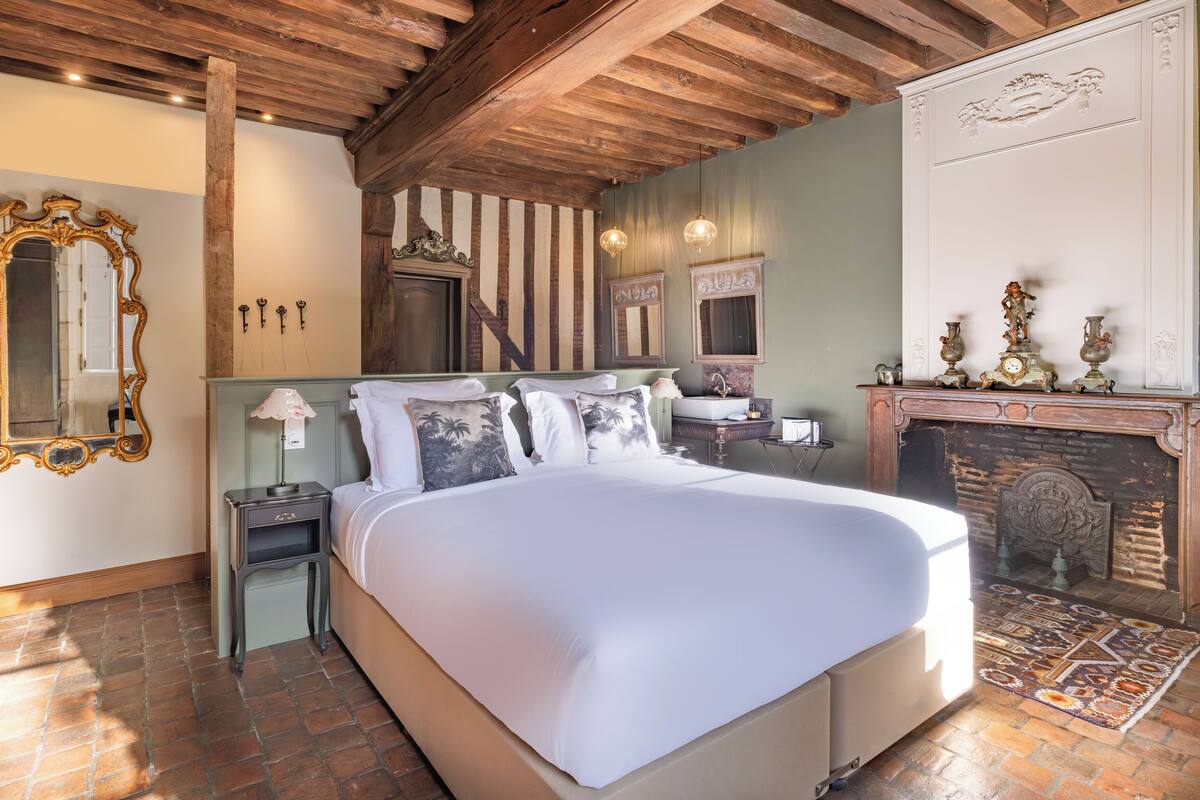 Een slaapkamer met een groot bed, houten plafond, open haard en een spiegel.