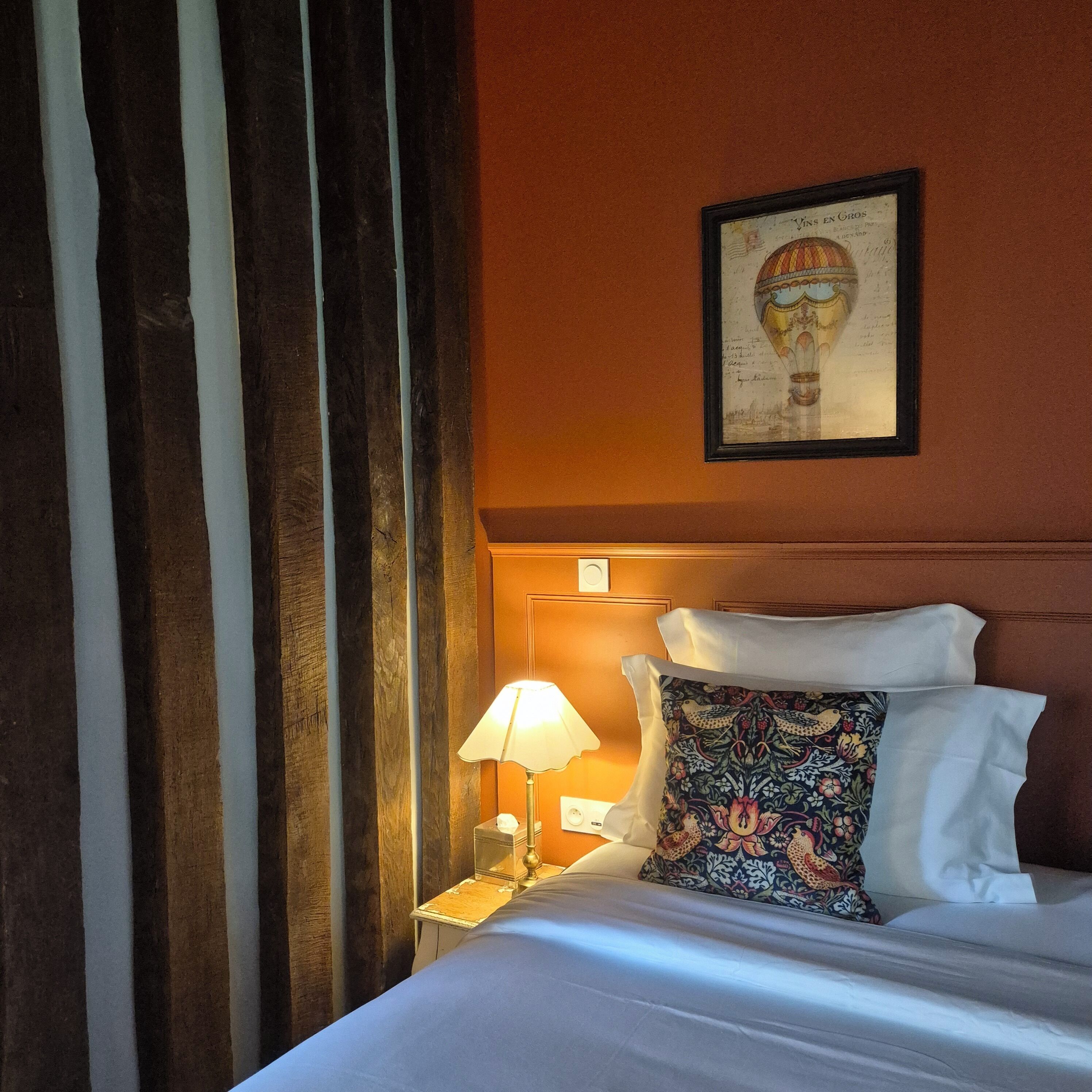 Een hotelkamer met een bed, een nachtkastje met een lamp, een ingelijst schilderij aan de muur en een raam met gordijnen.