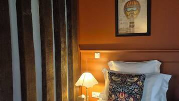Een hotelkamer met een bed, een nachtkastje met een lamp, een ingelijst schilderij aan de muur en een raam met gordijnen.