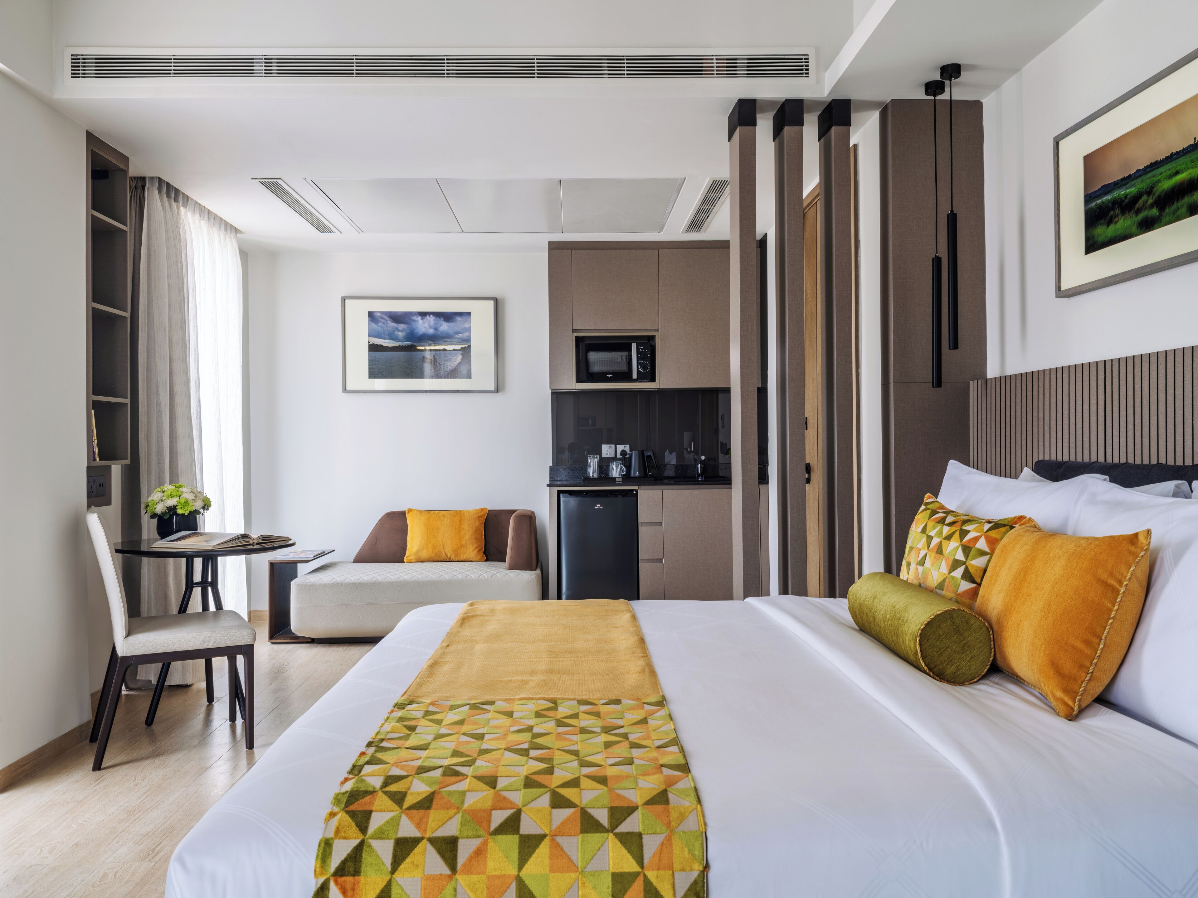 A hotel room with a large bed, a desk with a chair, a kitchenette, and a view of the outdoors.