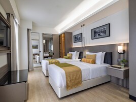 Una habitación de hotel moderna con dos camas, un espejo grande, un tocador con lavabo y una mesita de noche con lámpara.