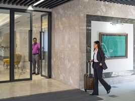 Un moderno vestíbulo de hotel con piso de mármol, puerta de cristal y una obra de arte enmarcada en la pared.