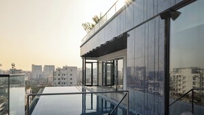 A rooftop infinity pool with lounge chairs, a modern building with large windows, and a cityscape view in the background. - W Residence Living (Dhaka)