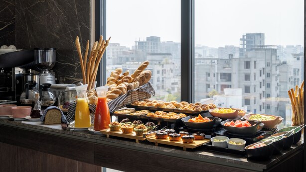 A breakfast buffet with various pastries, fruits, and beverages, set against a city view. - W Residence Living (Dhaka)