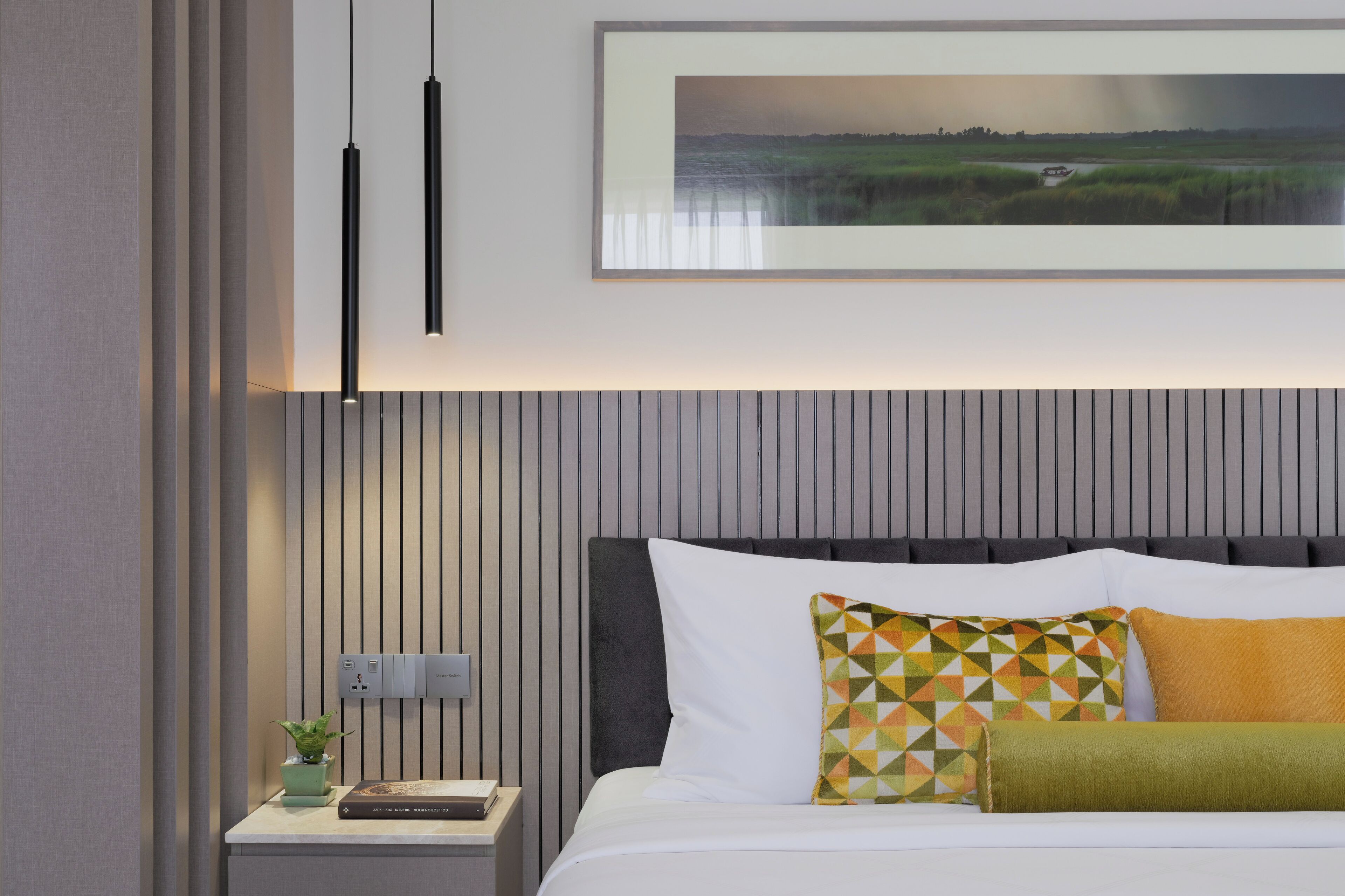 A modern bedroom with a bed, a nightstand, a framed landscape painting, and a pendant light.