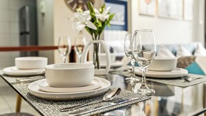 A dining table set with white plates, bowls, and cutlery, accompanied by a vase of white flowers and two wine glasses. - Tourist neighborhood 1 block from the subway (Santiago)