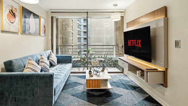 A modern living room with a grey sofa, a coffee table, and a large flat-screen TV displaying 'NETFLIX'. - Tourist neighborhood 1 block from the subway (Santiago)