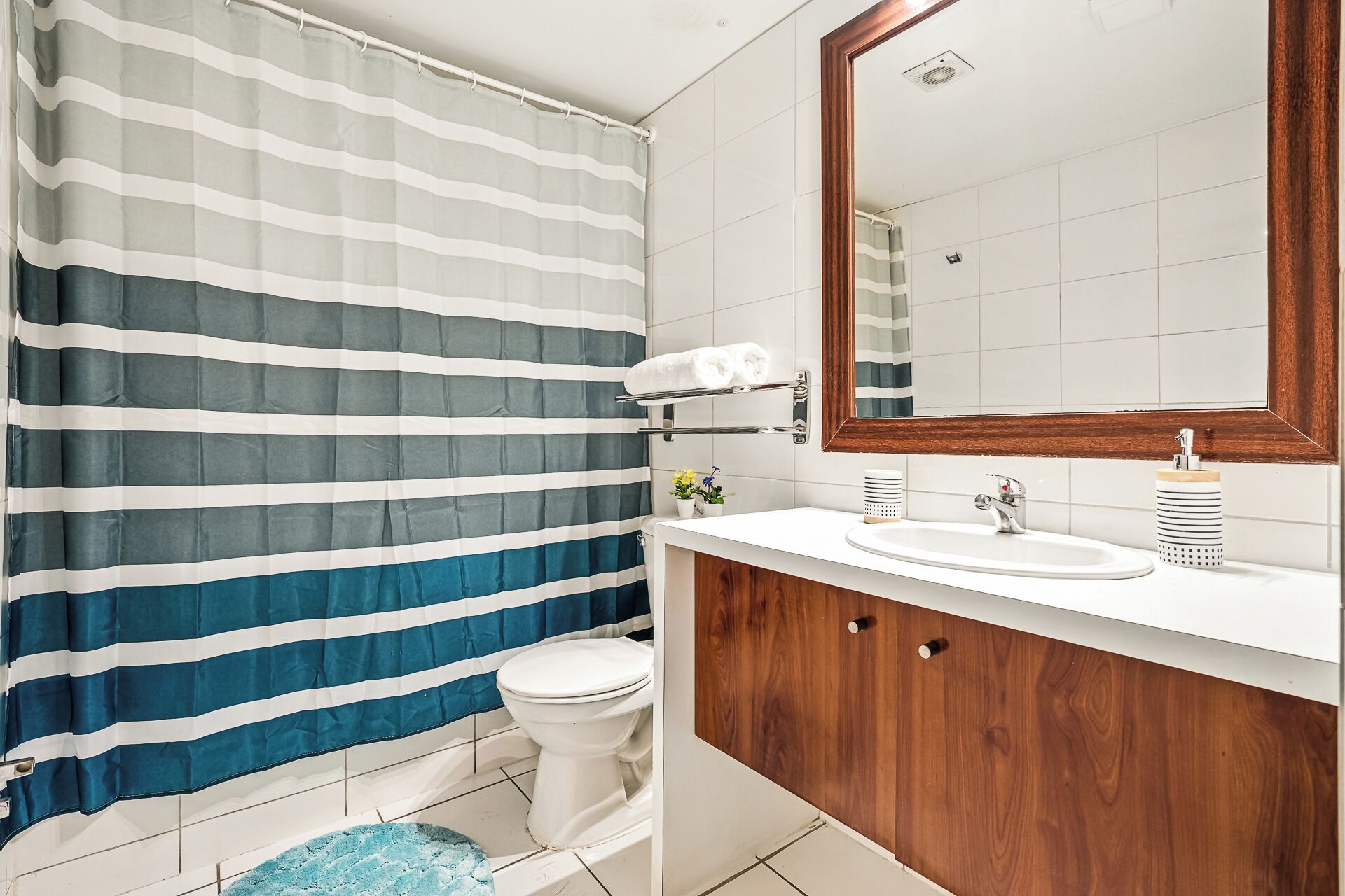 A bathroom with a striped shower curtain, a toilet, a sink with a mirror, and a wooden vanity.