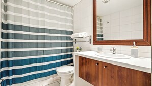 A bathroom with a striped shower curtain, a toilet, a sink with a mirror, and a wooden vanity. - Tourist neighborhood 1 block from the subway (Santiago)