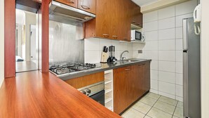A kitchen with wooden cabinets, a gas stove, a microwave, and a refrigerator. - Tourist neighborhood 1 block from the subway (Santiago)
