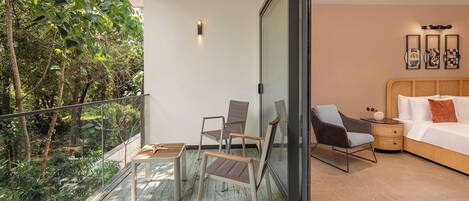 Un dormitorio moderno con una cama grande, una mesita de noche y una zona de estar con sillas. Cuenta con un balcón con puerta de cristal que da a un jardín.