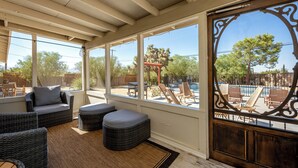 A sunlit patio with wicker furniture, large windows, and a view of a pool and outdoor area. - Family Retreat 3BR InGround Pool + Spa+ Private fenced back yard+Sun Room. (Yucca Valley)