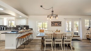 A spacious kitchen with a large island, bar stools, and a dining area with wooden chairs. - Family Retreat 3BR InGround Pool + Spa+ Private fenced back yard+Sun Room. (Yucca Valley)