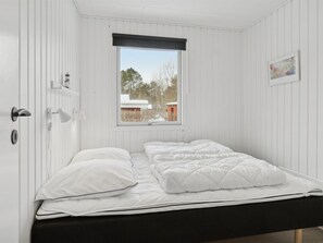 A bedroom with a bed, a window with a view, a door with a handle, and a wall-mounted light fixture.