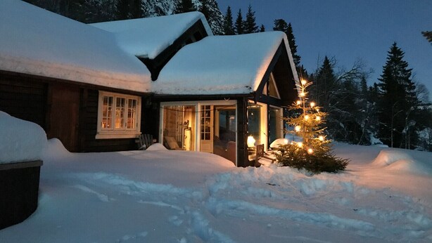 A log cabin with a snow-covered roof, a porch with a Christmas tree, and a mountain backdrop. - Winter and summer lodge for adventures, wilderness experience in the N.mountains (Innlandet)