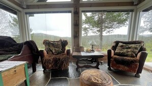 A cozy room with a stone floor, two fur-covered chairs, a wooden table, and a view of a forest through large windows. - Winter and summer lodge for adventures, wilderness experience in the N.mountains (Innlandet)