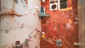 Une salle de bain avec un mur en marbre, une douche, des toilettes et un seau bleu.