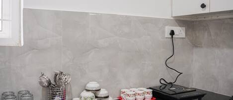 A kitchen with a black countertop, a coffee maker, and a set of teapots and cups.