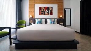 A modern hotel room with a large bed, a wooden headboard, a colorful abstract painting, two bedside tables with lamps, and a green chair. - TreeHouse Velis Sonipat (Ganaur)