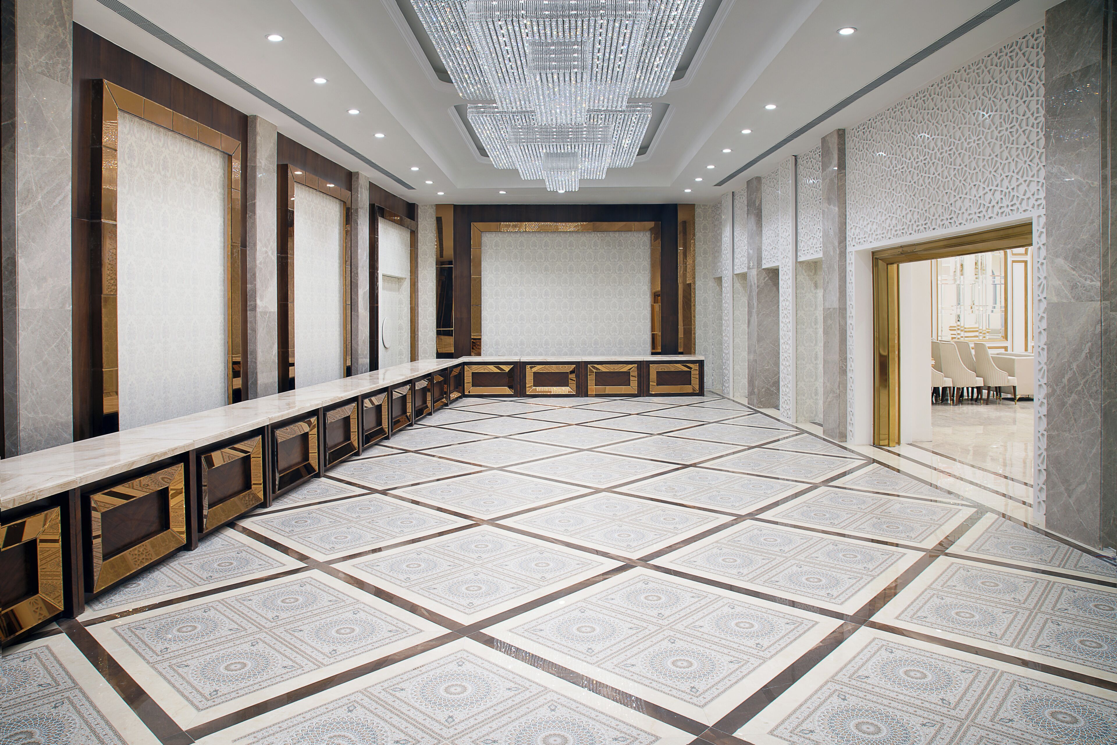 A spacious lobby with a long reception desk, patterned floor tiles, and a large chandelier.