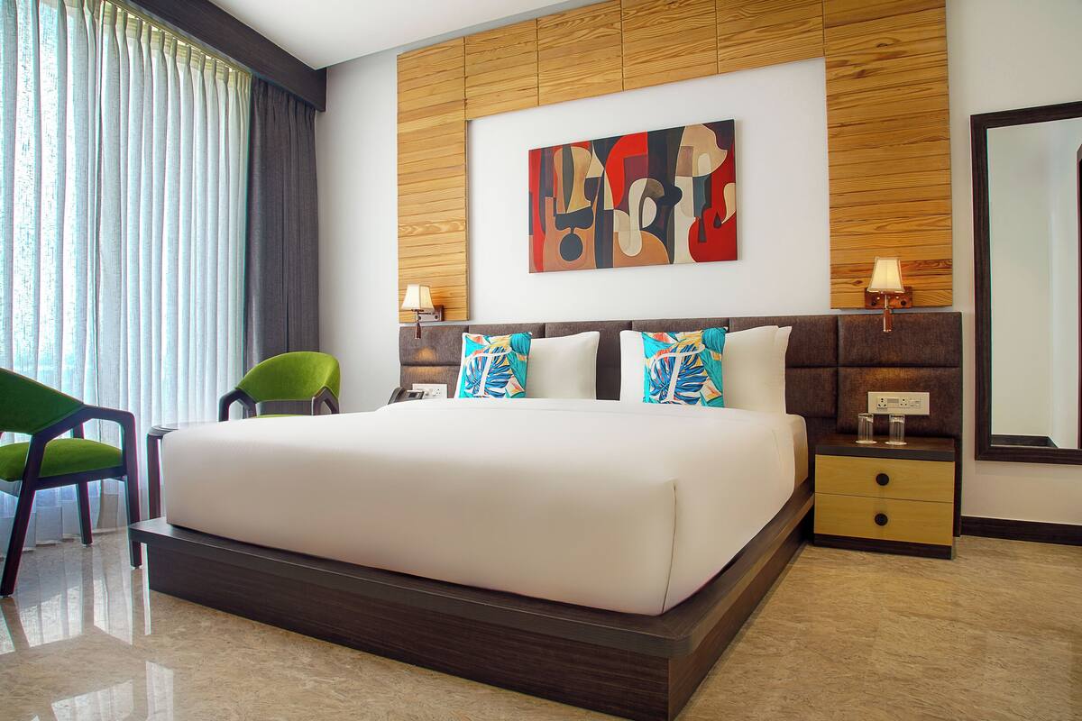 Una habitación de hotel moderna con una cama grande, un cabecero de madera, un cuadro, una mesita de noche, una lámpara y una silla.