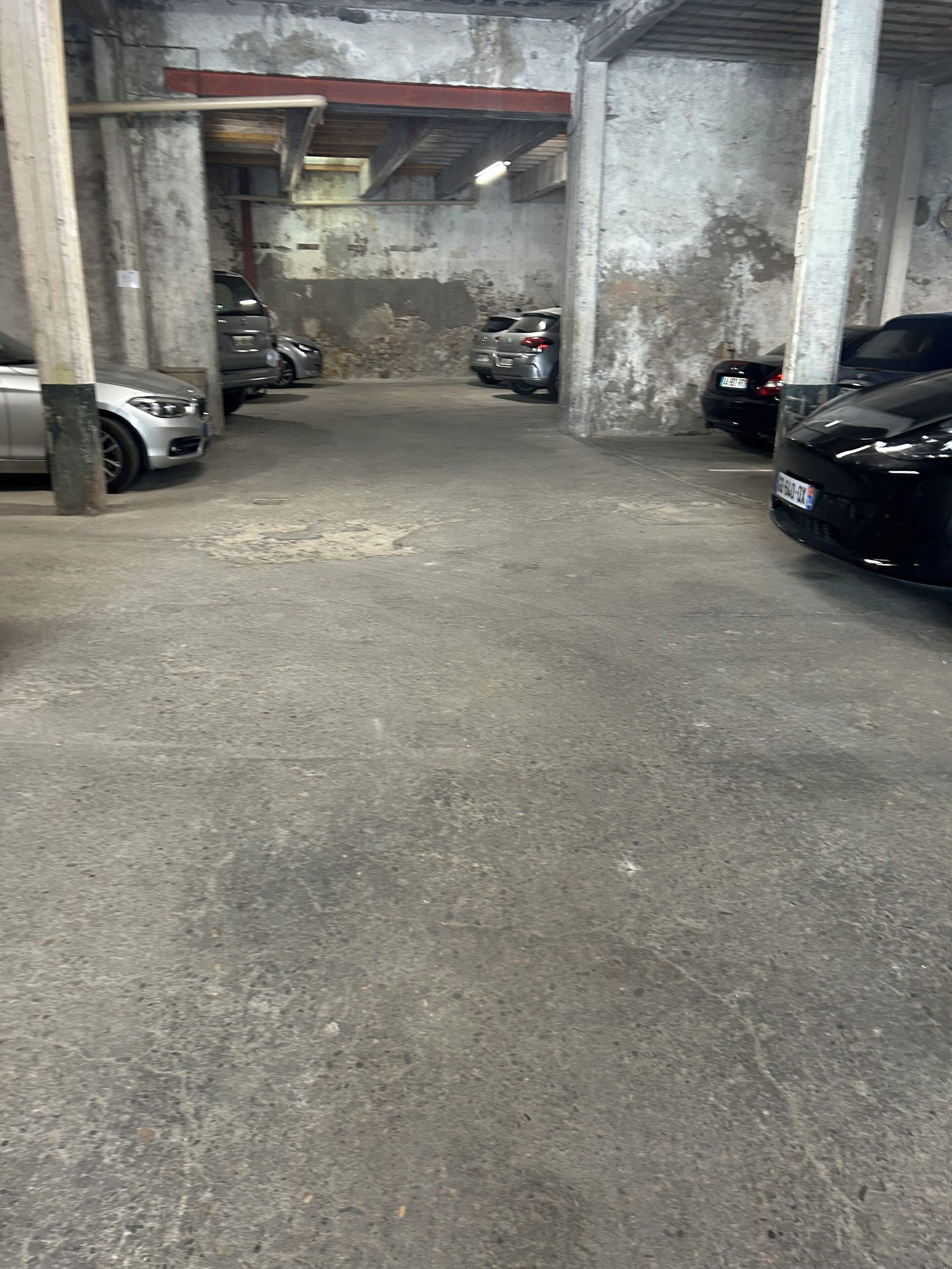 Un garaje de estacionamiento con pisos y paredes de concreto, mostrando varios automóviles estacionados.