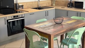 Une cuisine moderne avec une table en bois, des chaises vertes, un four encastré et un four à micro-ondes.