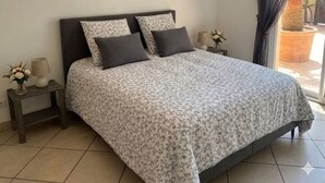 Une chambre à coucher avec un lit, une table de chevet, une horloge murale et une fenêtre avec des rideaux.
