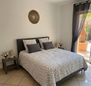 Quarto com cama, mesa de cabeceira, relógio de parede e janela com cortinas.