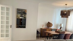 Un salon moderne avec un canapé d’angle, un coin repas doté d’une table en bois et un tableau accroché au mur.
