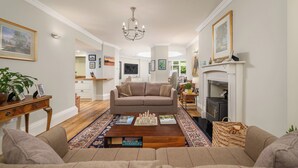 A living room with a beige sofa, a coffee table with books, a fireplace, and a chandelier.