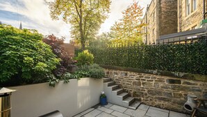 A stone staircase leading up to a building, surrounded by lush greenery and a metal fence.