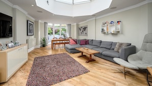 A spacious living room with a large skylight, a grey sofa, a wooden coffee table, and a colorful rug.