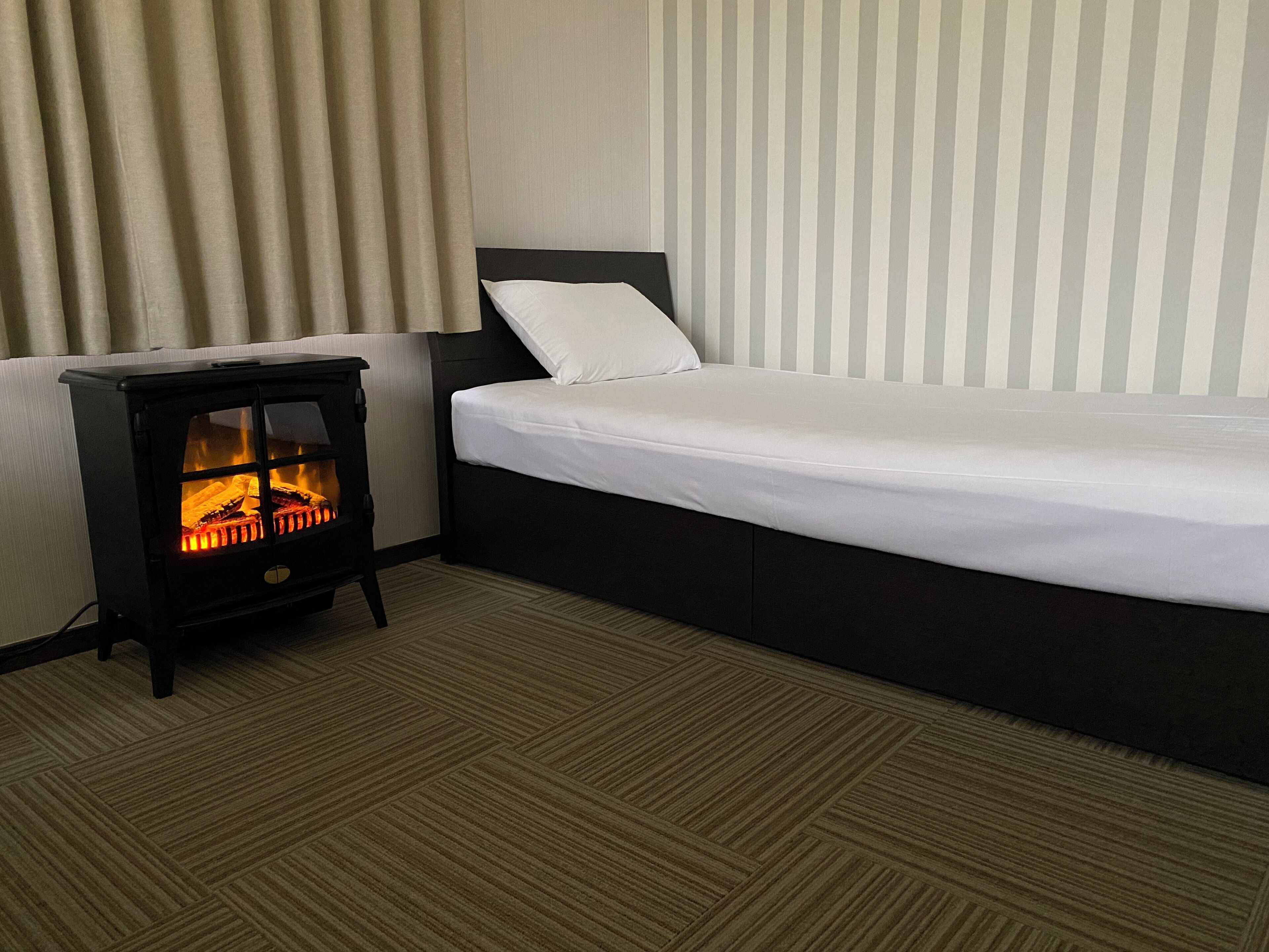 Una camera d'albergo con un letto, un piccolo termosifone nero e un muro a righe.