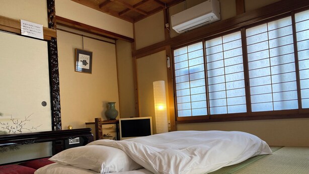 A traditional Japanese room with tatami flooring, a bed with white bedding, a TV, and a window with shoji screens. - The whole building can be rented (only for guests) Long term welcome Outlet 7 min walk 11 people 1 bedding per person, no hassle Max 12 people, clean, spacious with Japanese style rooms 4 free parking spaces 4 bedrooms BBQ reservations possible (木更津市)