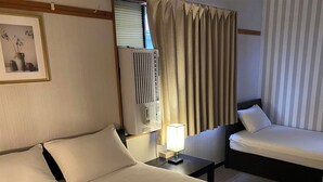 Une chambre d’hôtel avec un grand lit, un lit plus petit, une table de chevet avec une lampe, une fenêtre avec des rideaux et un tableau encadré au mur.