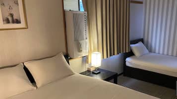Camera d'albergo con un letto grande, un letto più piccolo, un comodino con una lampada, una finestra con tende e un quadro appeso al muro.