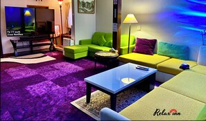 Una sala de estar moderna con televisor, sofás verde y amarillo, una mesa de centro y una alfombra púrpura.