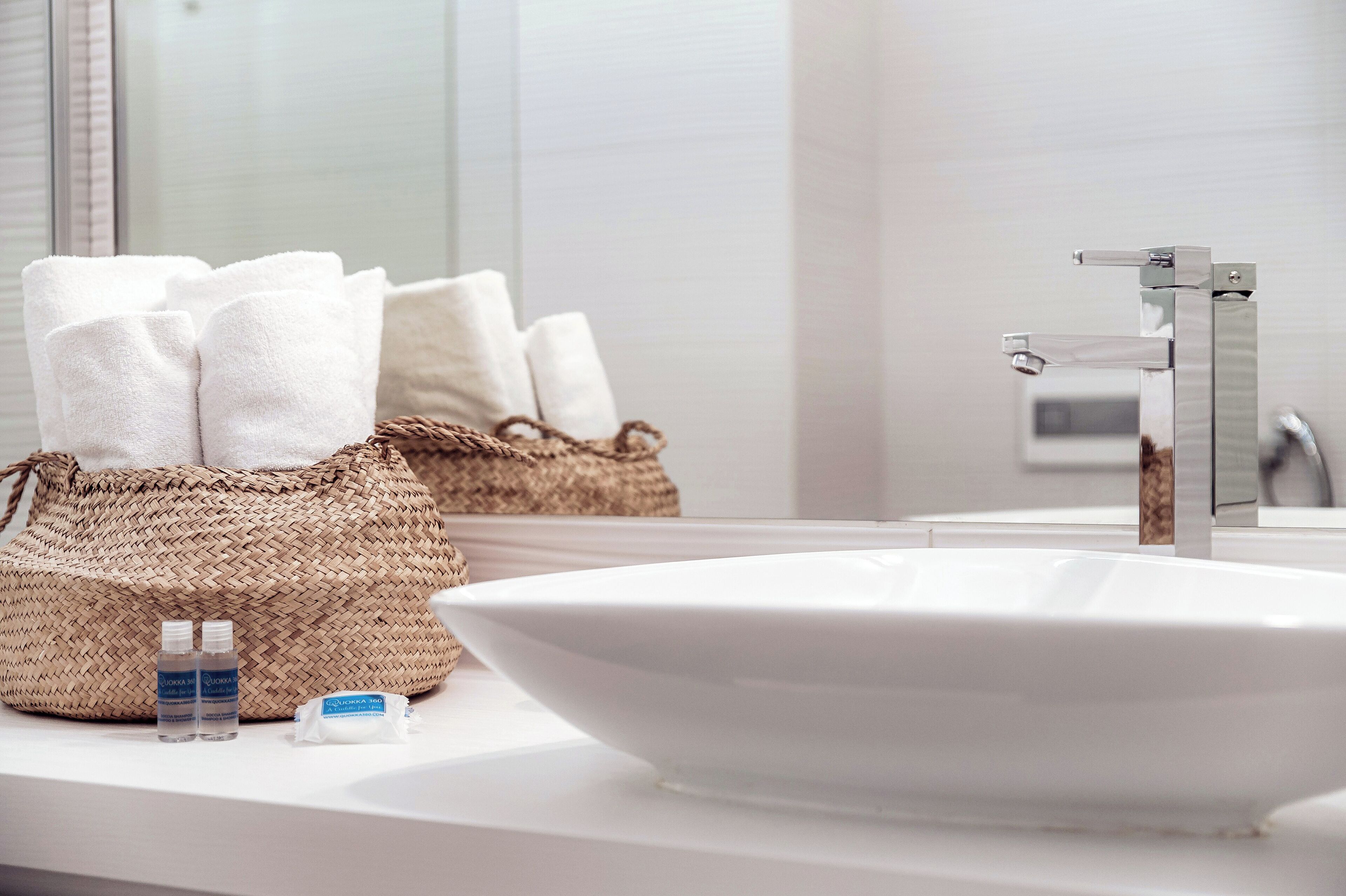 Ein Badezimmer mit einem großen, weißen Waschbecken, einem gewebten Korb mit Handtüchern und Pflegeprodukten auf der Ablagefläche.
