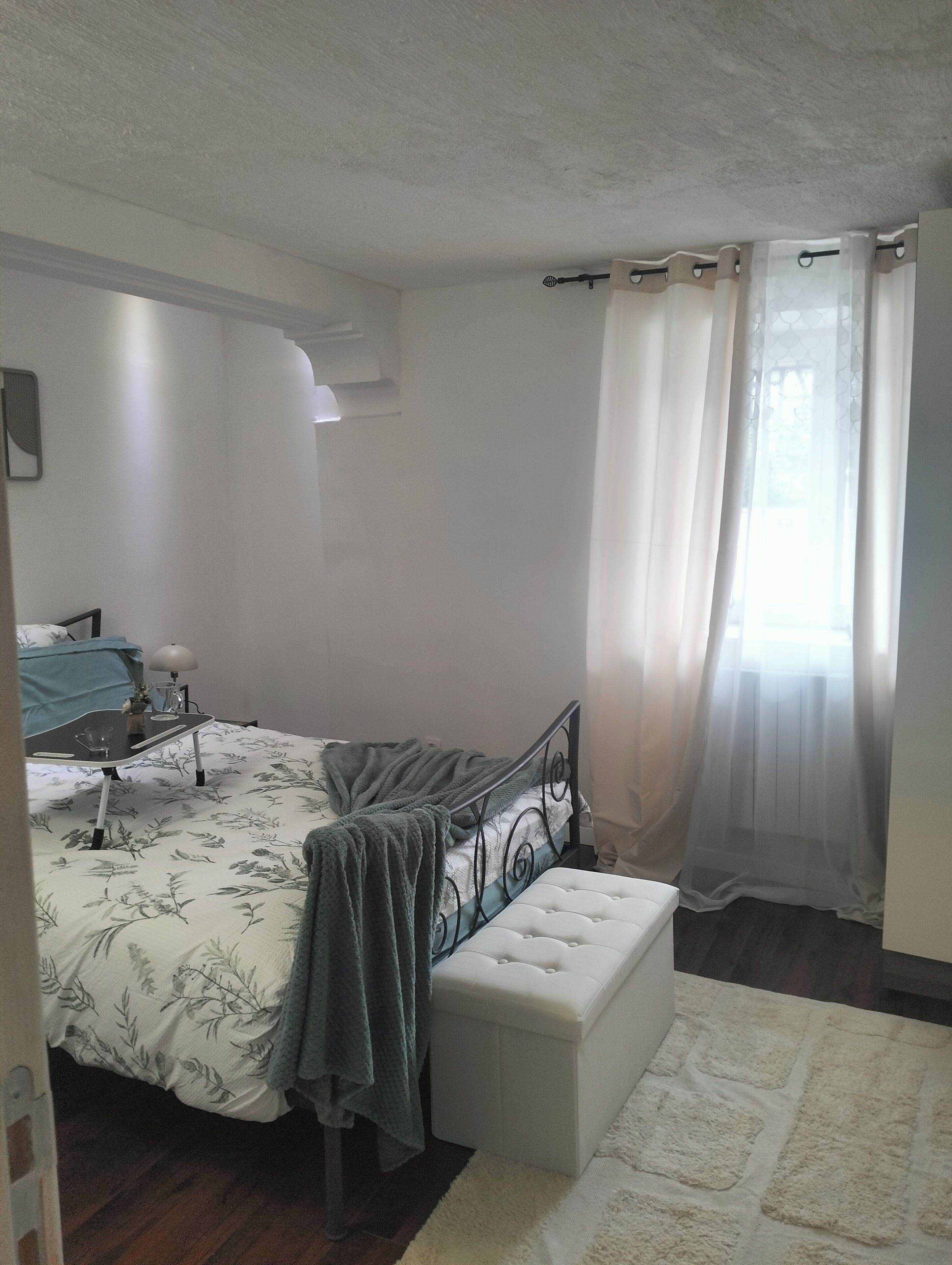 Une chambre à coucher avec un lit, une table de chevet, une lampe et une fenêtre avec des rideaux.