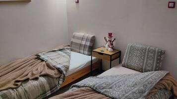 Een kleine, gezellige kamer met twee eenpersoonsbedden, een nachtkastje met een lamp en twee afbeeldingen in lijsten aan de muur.