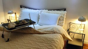 A neatly made bed with a white quilt, two bedside lamps, and a small table with a swan figurine and a candle. - Bright apartment in Mertzwiller (Mertzwiller)