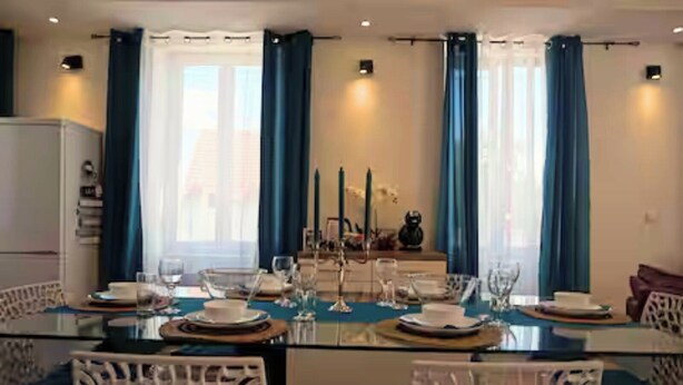 A dining area with a glass table set for four, blue curtains, and white chairs. - Bright apartment in Mertzwiller (Mertzwiller)