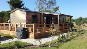 A wooden mobile home with a porch, a covered outdoor area, and a small garden. - Sfeervol chalet in Renesse met airco 3 slpk 2 badk (Renesse)