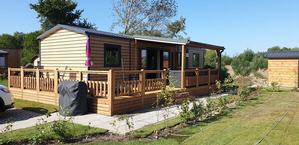A wooden mobile home with a porch, a covered outdoor area, and a small garden.