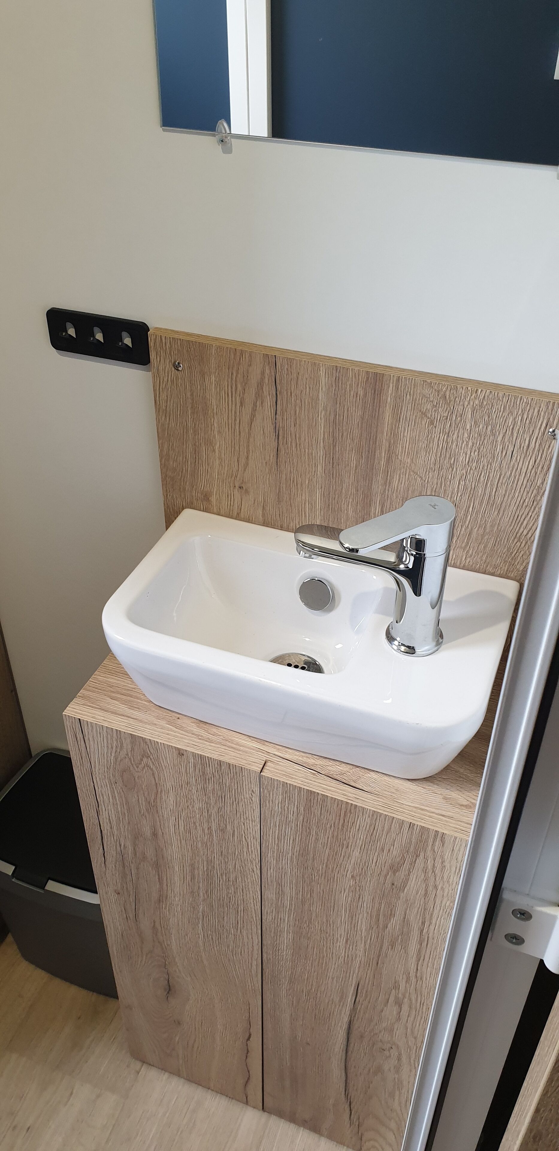 Un baño con lavamanos blanco, muebles de madera y un espejo sobre el lavamanos.
