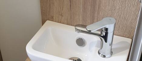 Un baño con lavamanos blanco, muebles de madera y un espejo sobre el lavamanos.