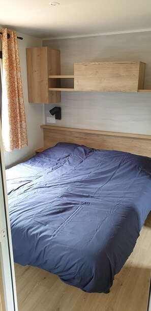 A room with a bed, wooden headboard, built-in shelves, and a curtain.