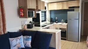 A compact kitchen with wooden cabinets, a microwave, a stove, a refrigerator, and a sink. - Sfeervol chalet in Renesse met airco 3 slpk 2 badk (Renesse)